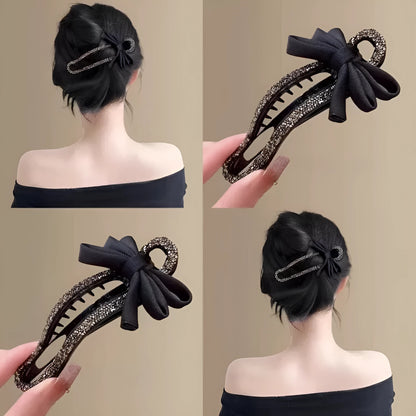 A black crystal bow on a clear 11.5cm long acrylic banana hair clip with bobby pin back.