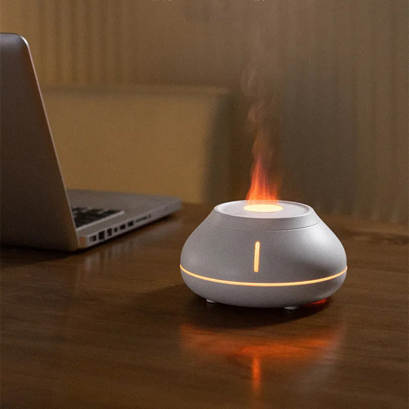 White rounded desktop aroma diffuser with colourful flame-like light and mist plume on a wooden table.