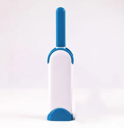 Blue reusable pet hair removal brush with double-sided head next to its self-cleaning base.