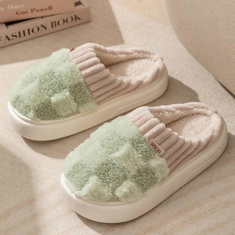 Plaid pattern women's plush slippers with coral velvet upper and textured PVC sole on a wooden floor.