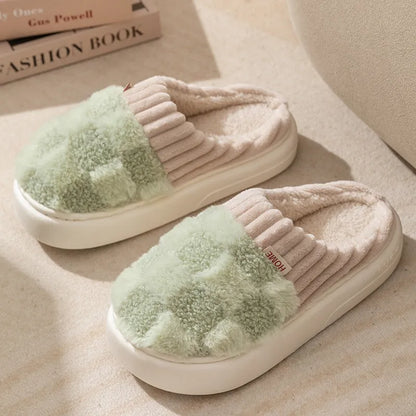 Plaid pattern women's plush slippers with coral velvet upper and textured PVC sole on a wooden floor.