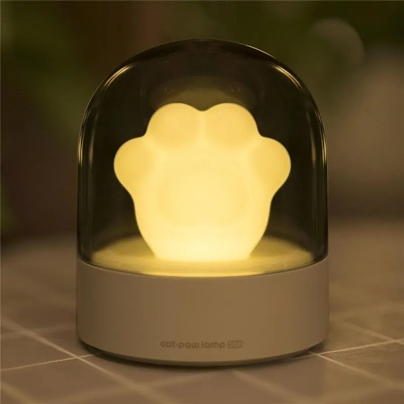 Grey cat paw shaped night light with USB port, glowing softly on a wooden surface.