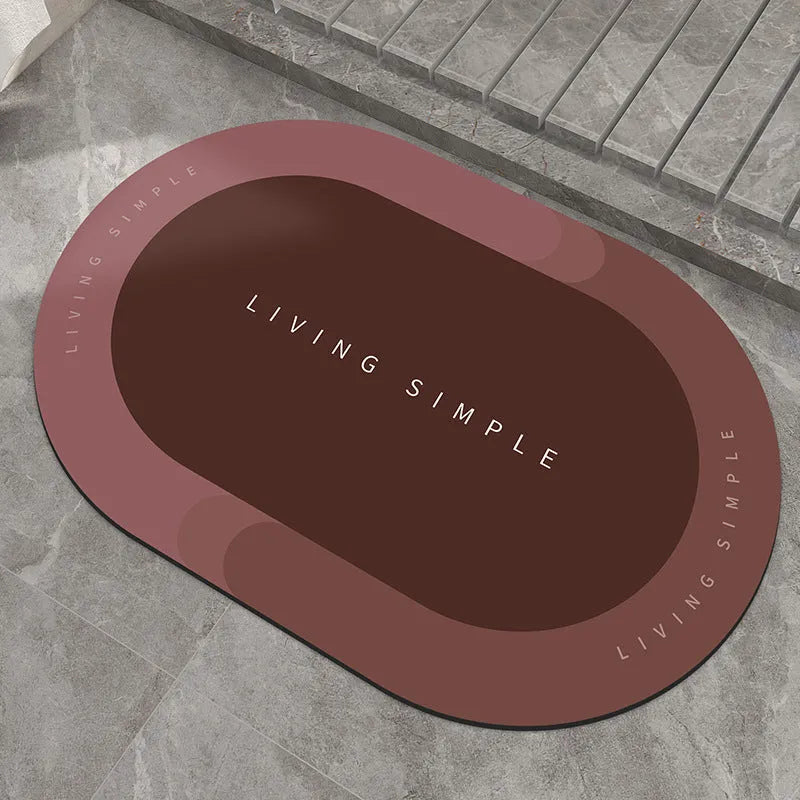 Oval grey bath mat with non-slip rubber bottom on a tiled floor, showing absorbent fabric surface