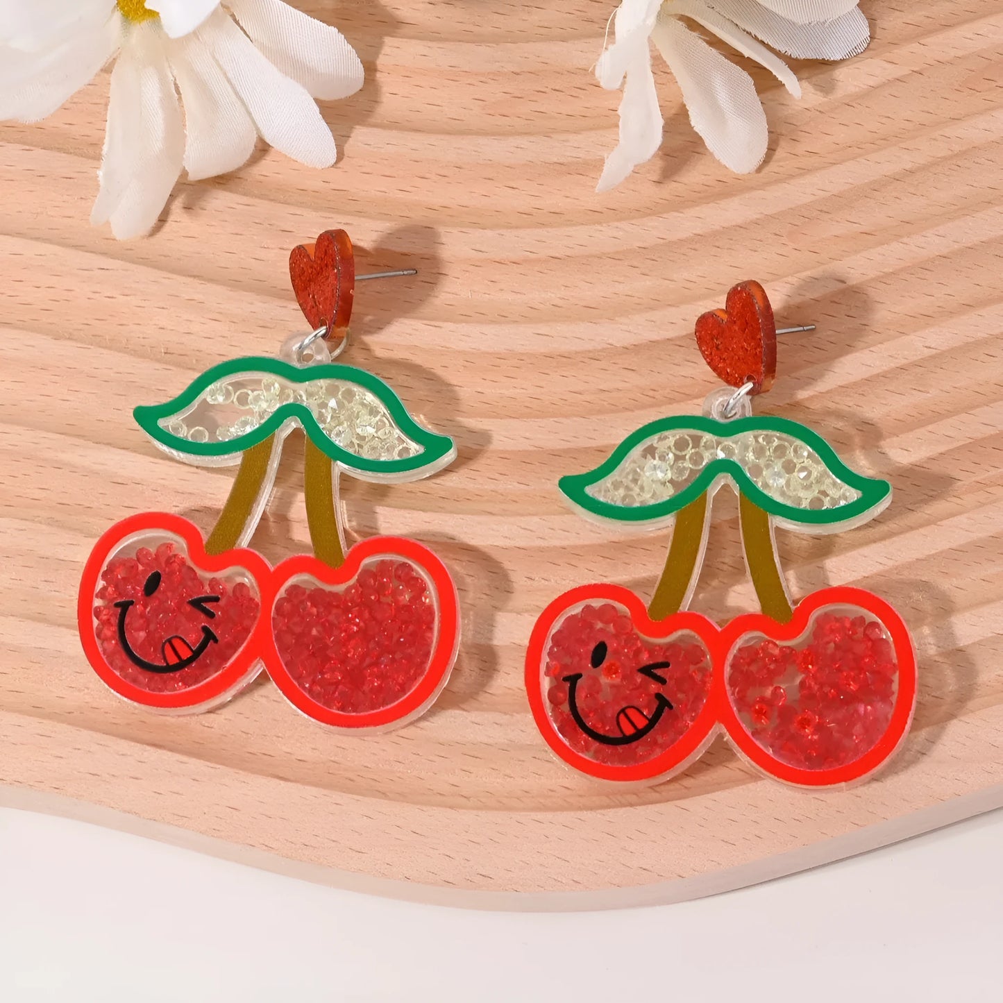 A pair of colourful acrylic earrings shaped like a strawberry and a cherry on a woman's ear.