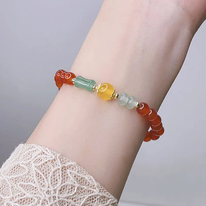 Close-up of a red agate bracelet with a dragon charm and Lucky Bag symbol on a wrist.