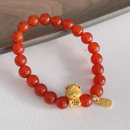 Close-up of a red agate bracelet with a dragon charm and Lucky Bag symbol on a wrist.