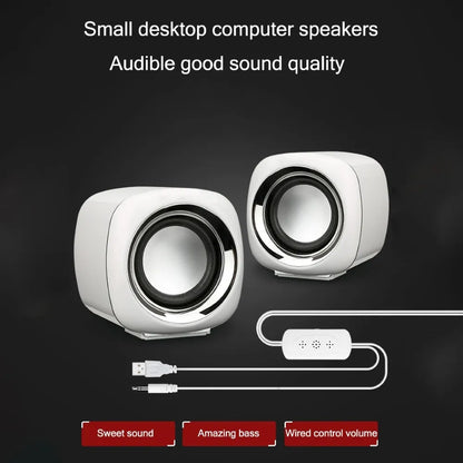 A pair of small black or white cube-shaped wired computer speakers with a 3.5mm audio plug on a desk.