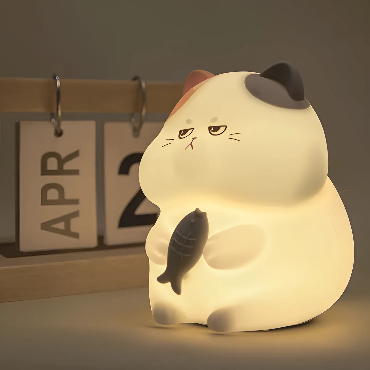 Yellow cartoon Greedy Cat desktop night light with plug, shown on a wooden desk.