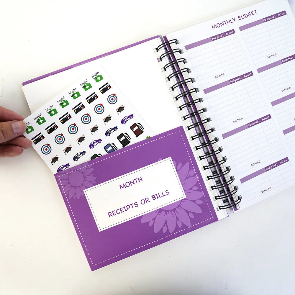 Purple coil-bound A5 budget notebook with pen, stickers and paper clips for financial planning