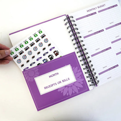 Purple coil-bound A5 budget notebook with pen, stickers and paper clips for financial planning