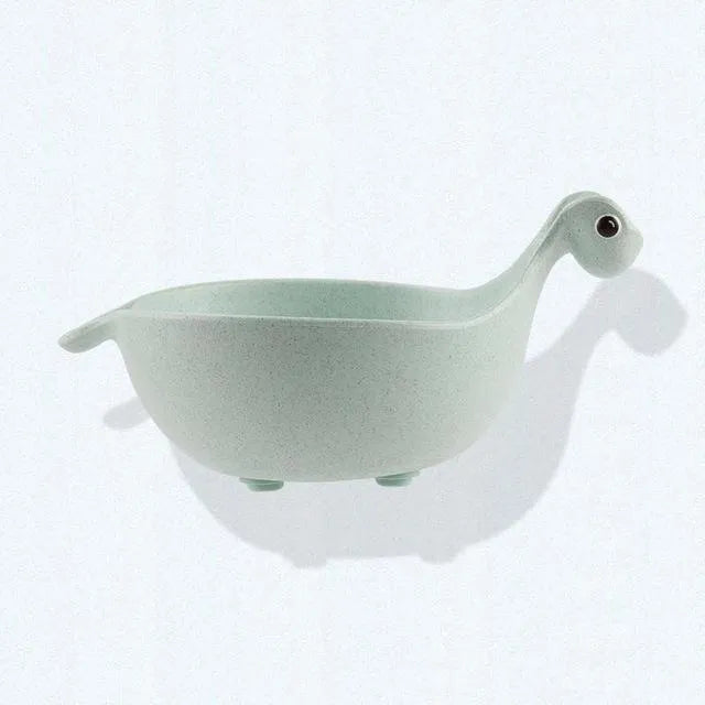 Three colourful dinosaur-shaped bowls made from wheat straw in pink, green, and beige.