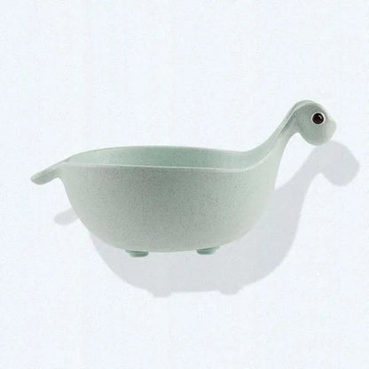 Three colourful dinosaur-shaped bowls made from wheat straw in pink, green, and beige.