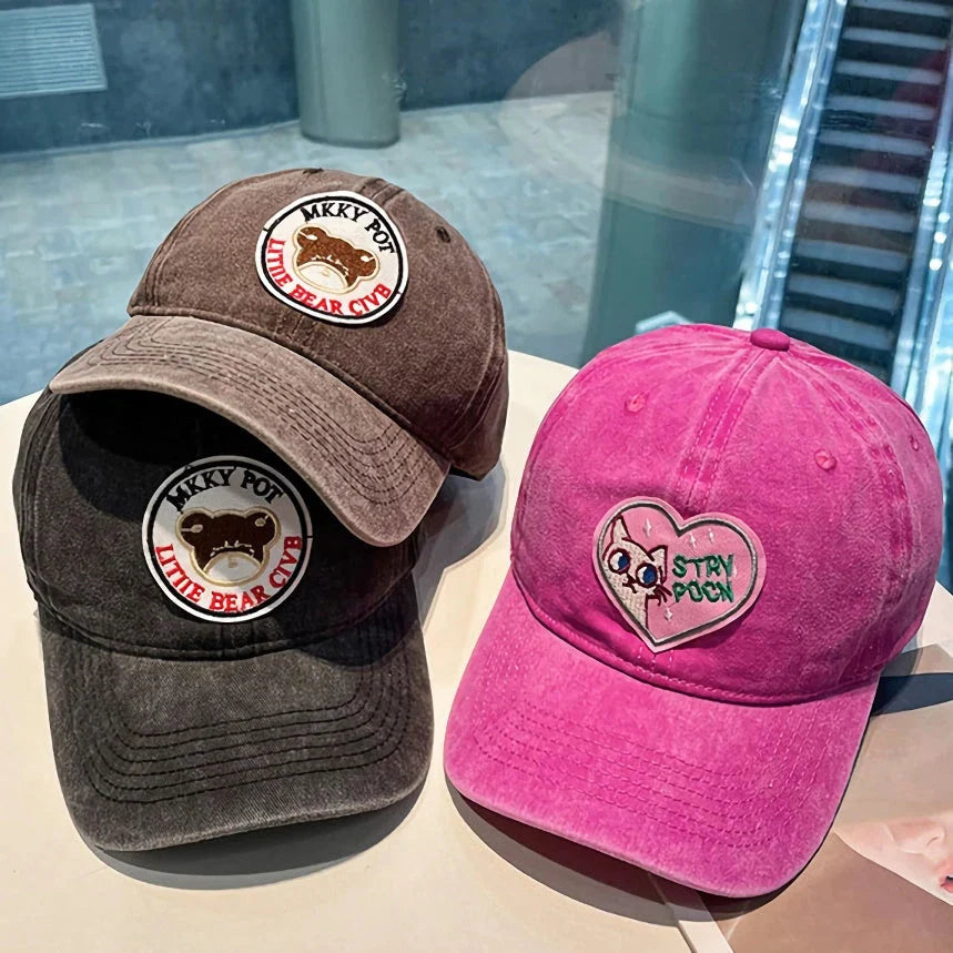 Two pink baseball caps featuring a cartoon love design, perfect for casual and festival wear
