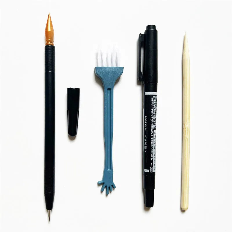 Diamond painting repair tool set with metal scraper pen, bottle of adhesive liquid, soft brush, and bamboo stick on a craft table