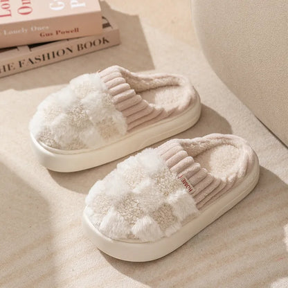 Plaid pattern women's plush slippers with coral velvet upper and textured PVC sole on a wooden floor.