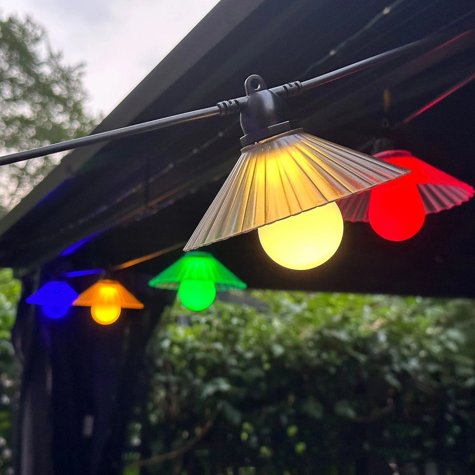 Outdoor LED string lights with white flower-shaped globes, shown illuminating a garden patio at dusk.