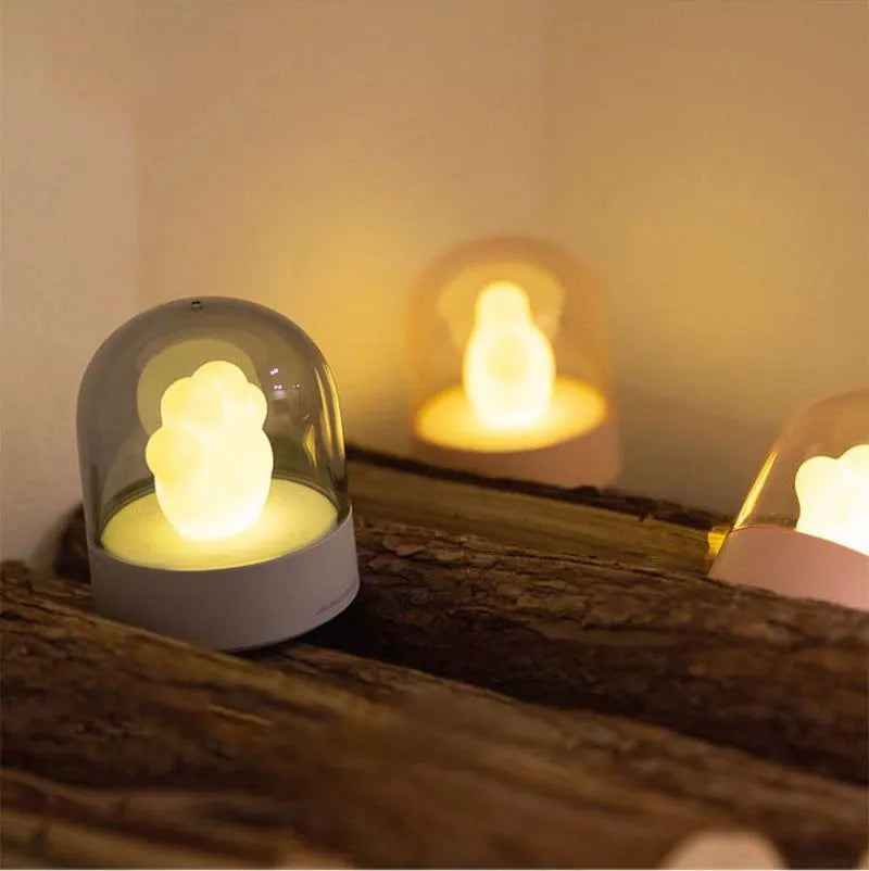 Grey cat paw night light with USB cable on a wooden desk, showing soft glow and detailed paw sculpt.