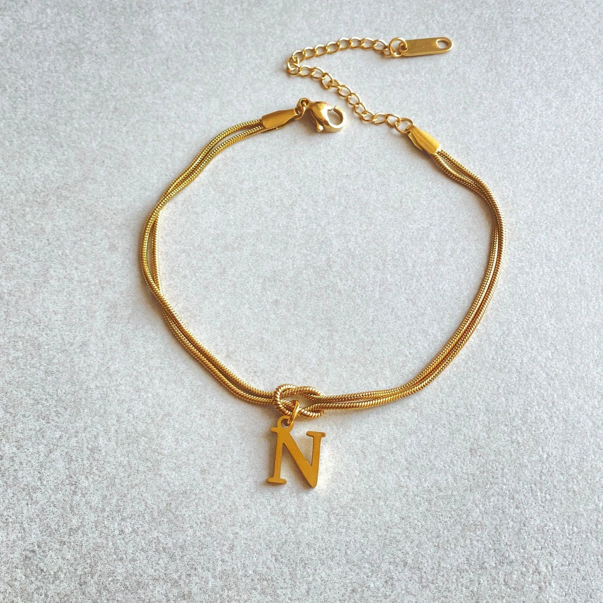Elegant letter charm bracelets for women in gold and silver tones, featuring a delicate snake chain design and personalised letter charms.