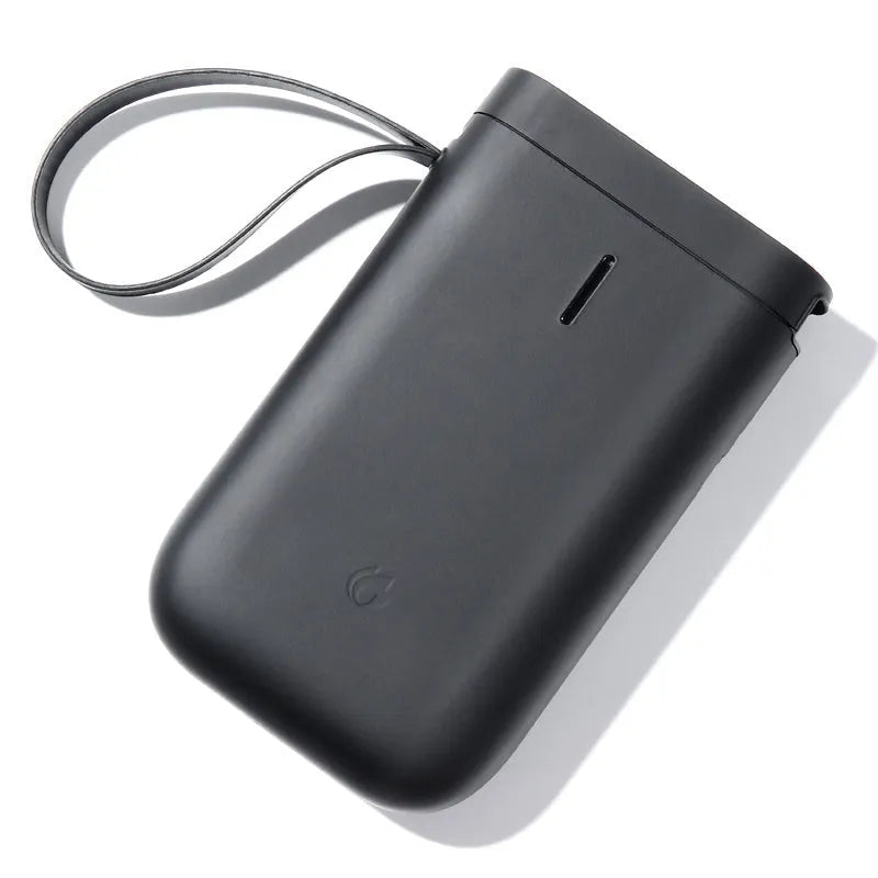 D11 black Bluetooth thermal label printer on a desk next to a smartphone showing the label design app