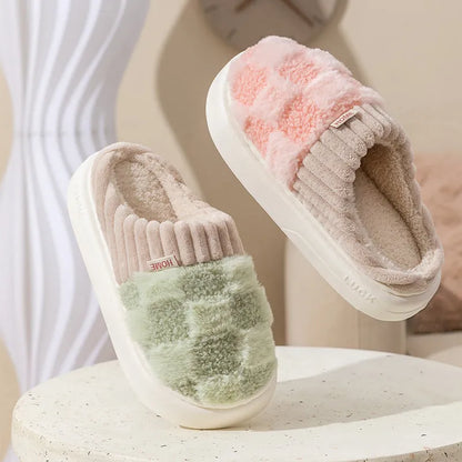 Plaid pattern women's plush slippers with coral velvet upper and textured PVC sole on a wooden floor.
