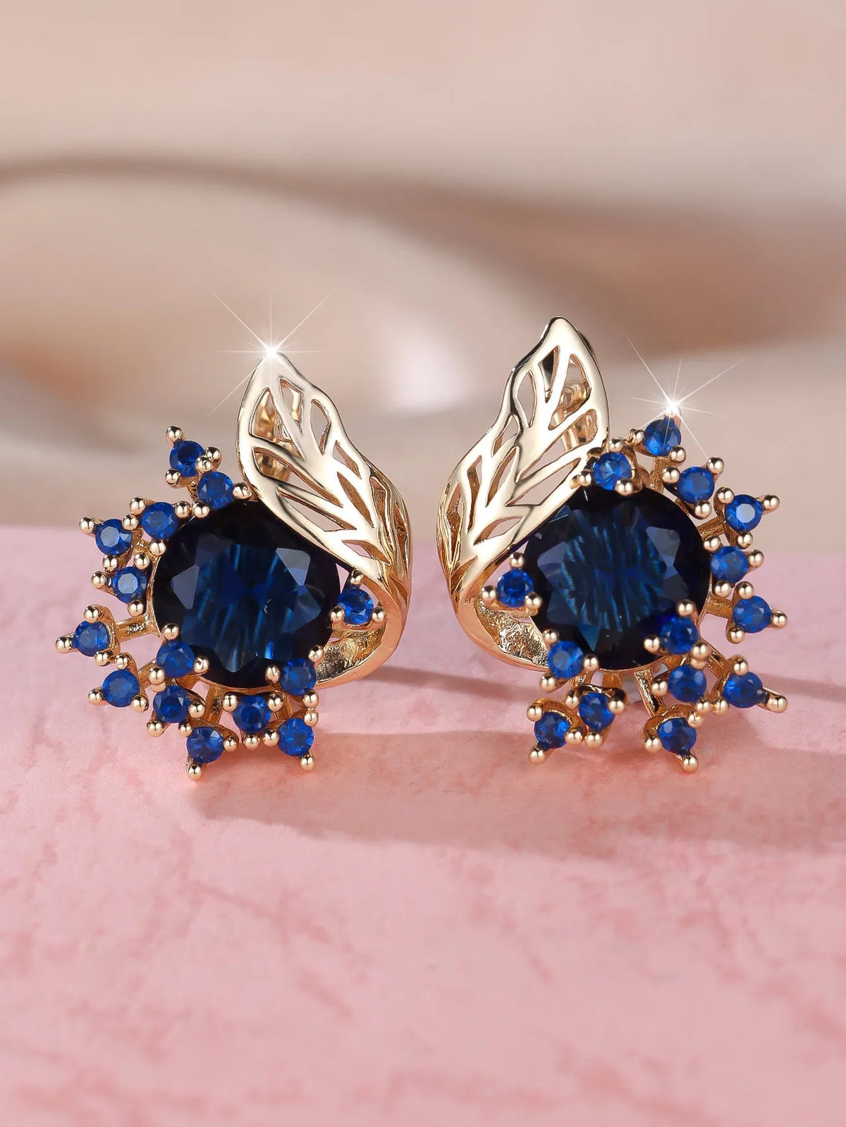 Rose gold plated women's stud earrings with a round flower shape, feather detail, and a central cubic zirconia stone.