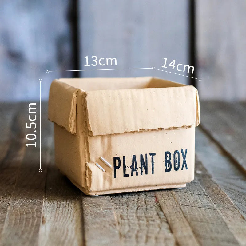 A grey cement flowerpot with a folded paper box design, shown with a drainage hole in its base.