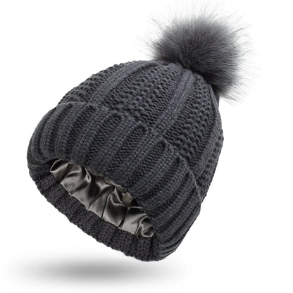 Woman wearing a wine red wool beanie hat with a faux fur pom pom and satin lining.