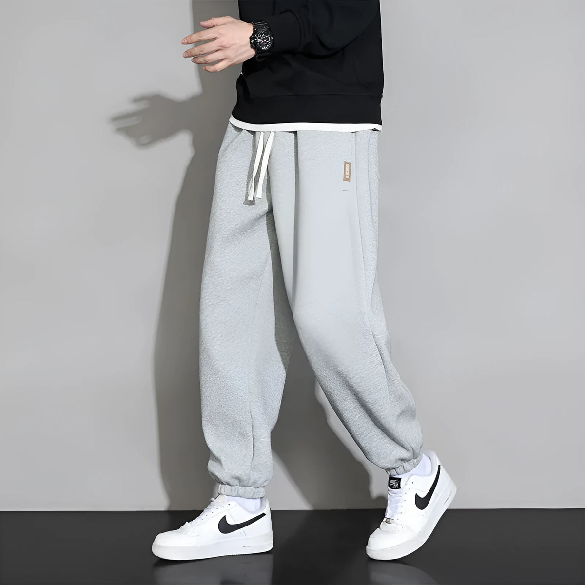 Man wearing loose grey sports trousers with an elasticated drawstring waistband.