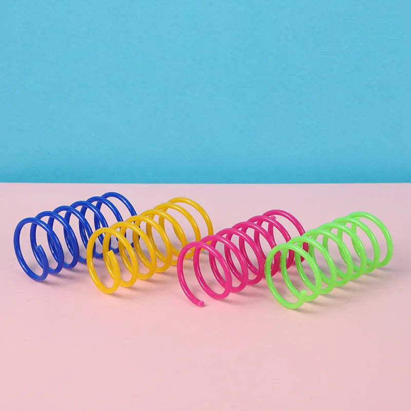 Assortment of colourful plastic coil spring toys for cats on a plain surface.