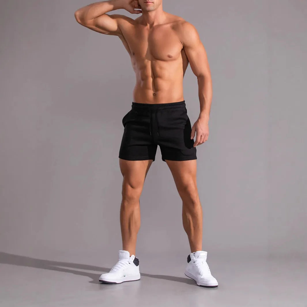 Three pairs of men's solid colour loose-fit drawstring shorts in black, khaki, and light brown laid flat.