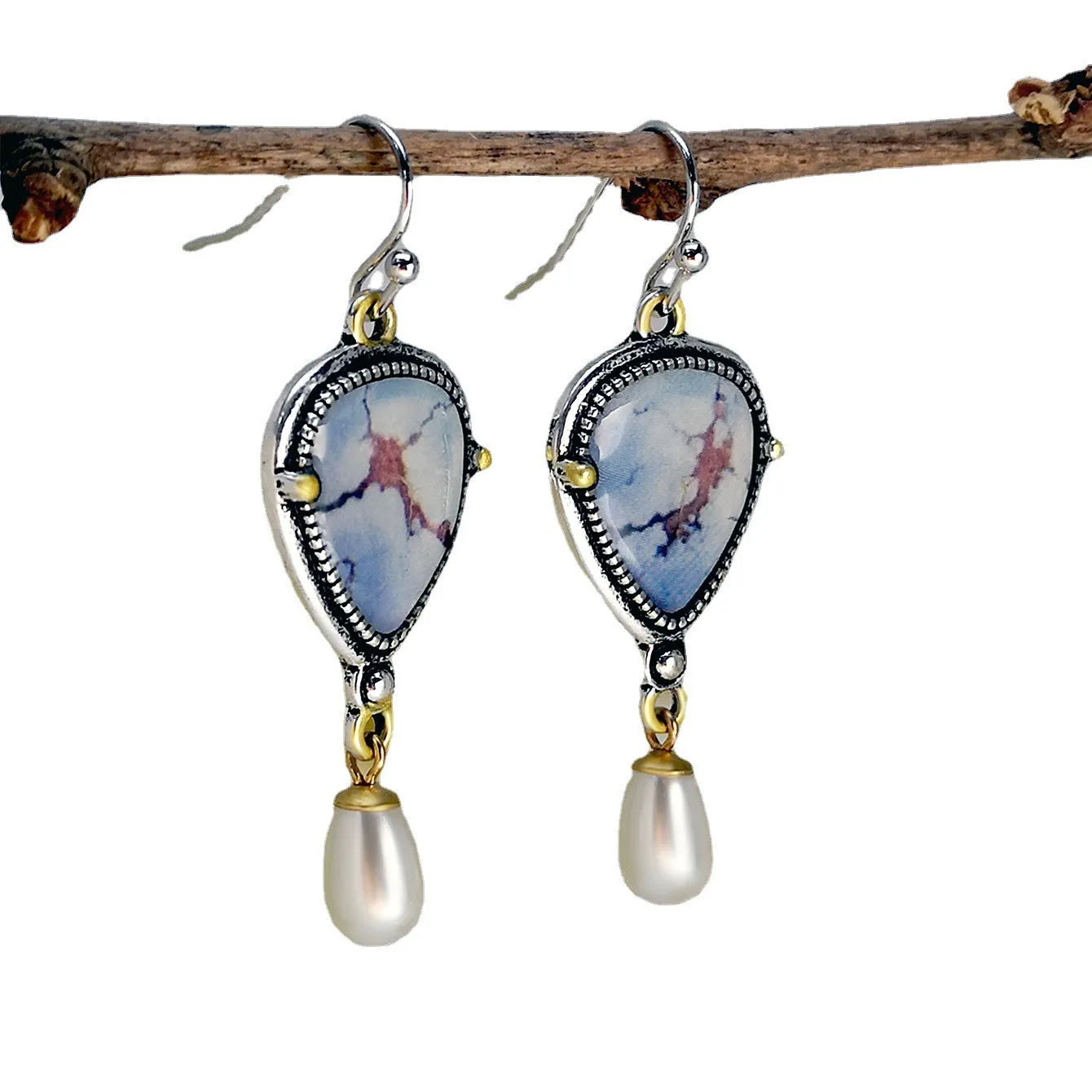 Close-up of retro blue geometric drop earrings with a synthetic blue opal stone and white pearl accent on an electroplated metal frame.