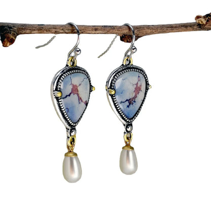 Close-up of retro blue geometric drop earrings with a synthetic blue opal stone and white pearl accent on an electroplated metal frame.