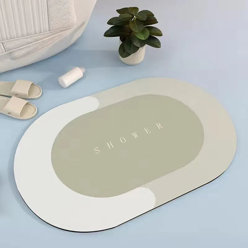 Oval grey bath mat with non-slip rubber bottom on a tiled floor, showing absorbent fabric surface
