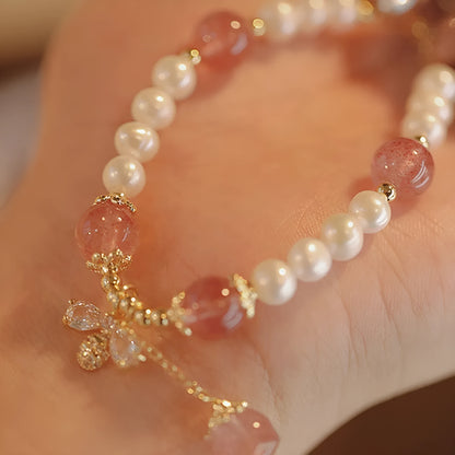 Women's strawberry quartz crystal bracelet with a decorative bow charm on a wrist.