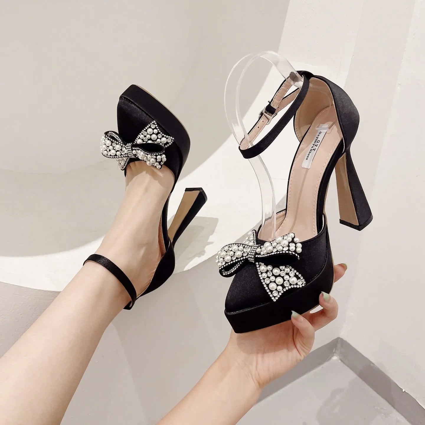 Women's black satin pointed-toe sandals with a bow detail on the front.