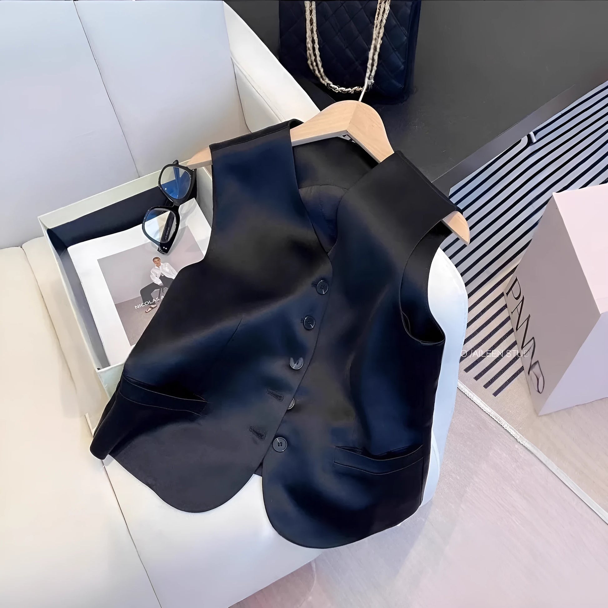 Black satin sleeveless vest on a hanger, showing loose fit and splicing detail.
