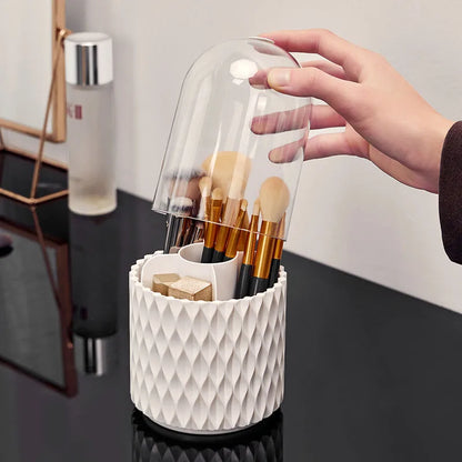 White rotating acrylic makeup brush holder with transparent dustproof lid on a desktop.