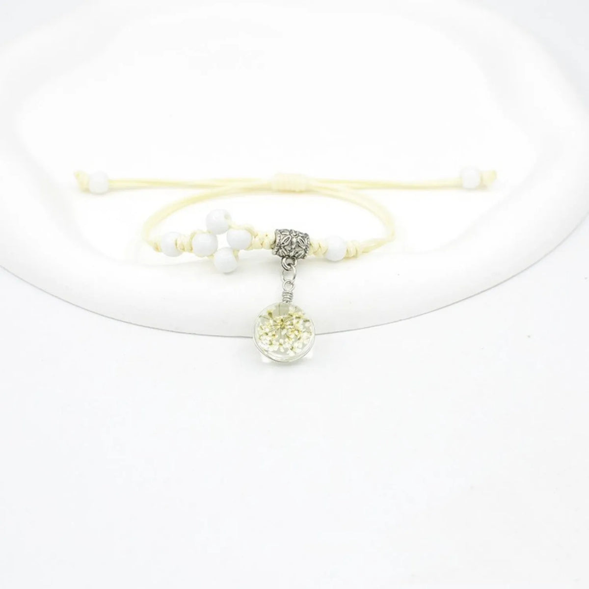 Close-up of a hand-woven bracelet with a large 1.4cm glass bead containing colourful dried flowers.