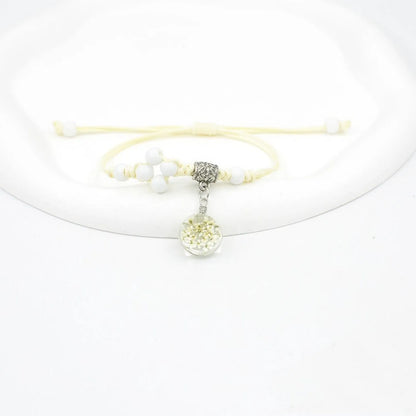 Close-up of a hand-woven bracelet with a large 1.4cm glass bead containing colourful dried flowers.