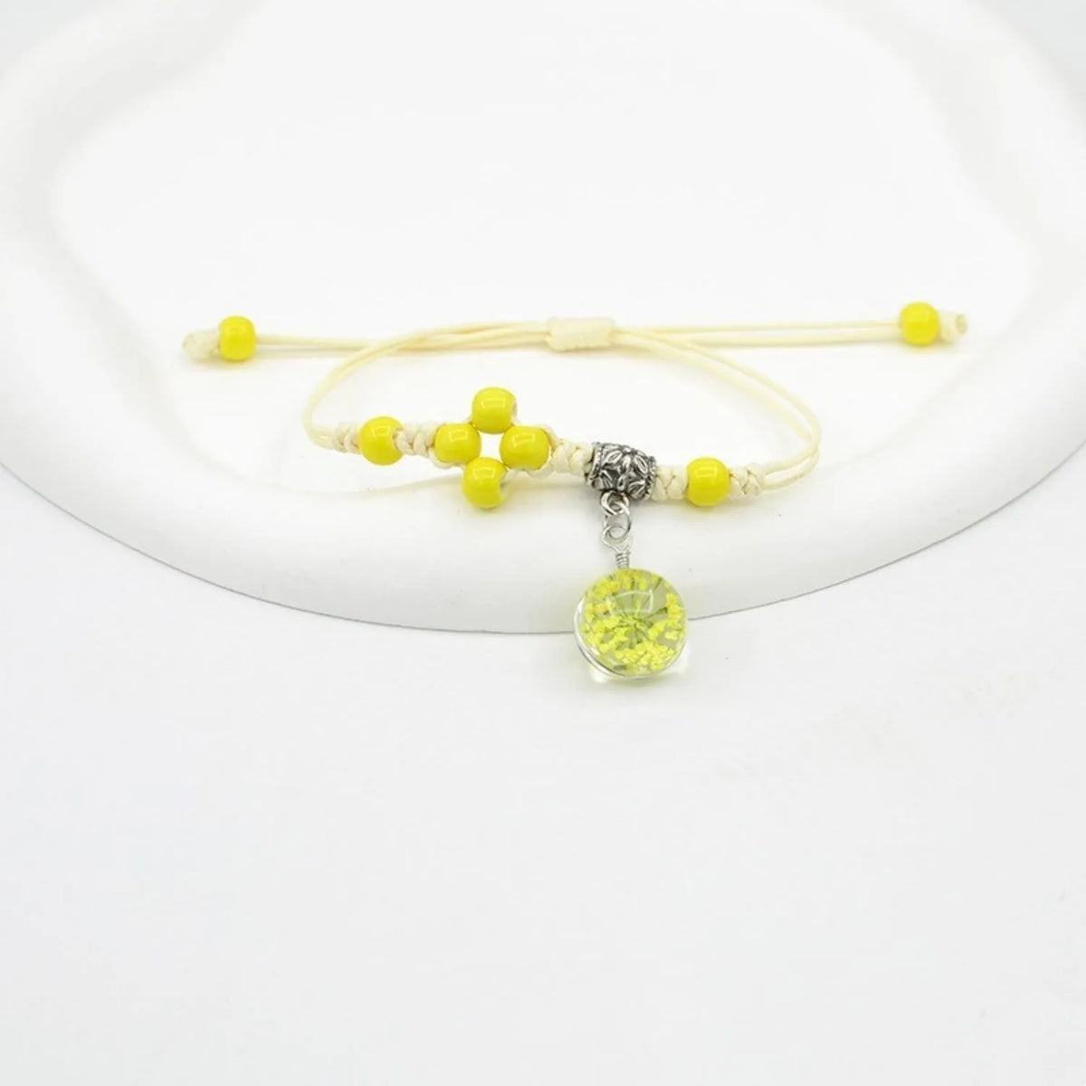 Close-up of a hand-woven bracelet with a large 1.4cm glass bead containing colourful dried flowers.