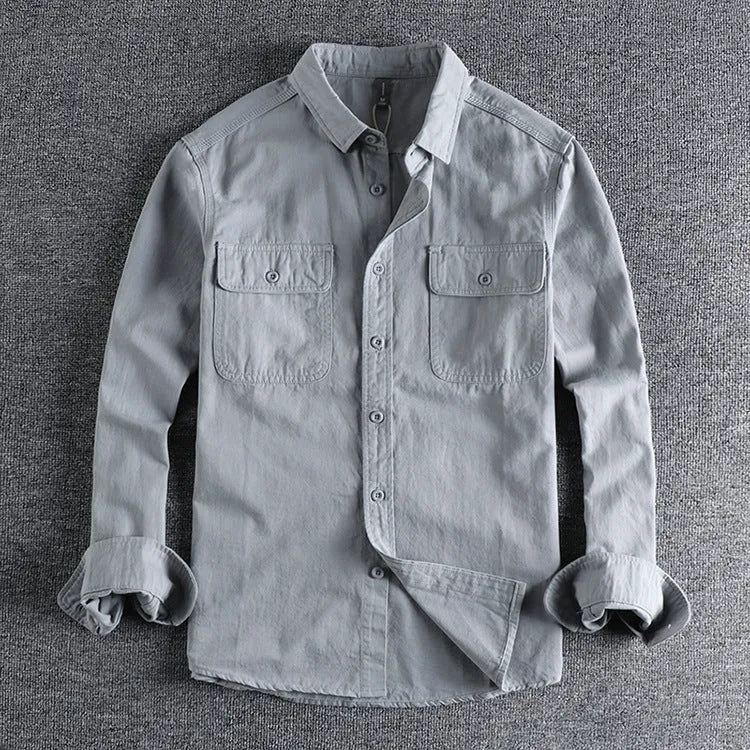 Man wearing a loose-fit grey cardigan-style overalls shirt with long sleeves.