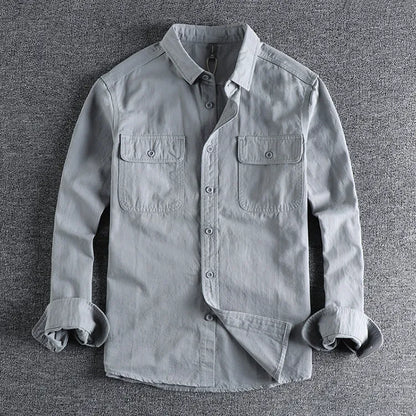 Man wearing a loose-fit grey cardigan-style overalls shirt with long sleeves.