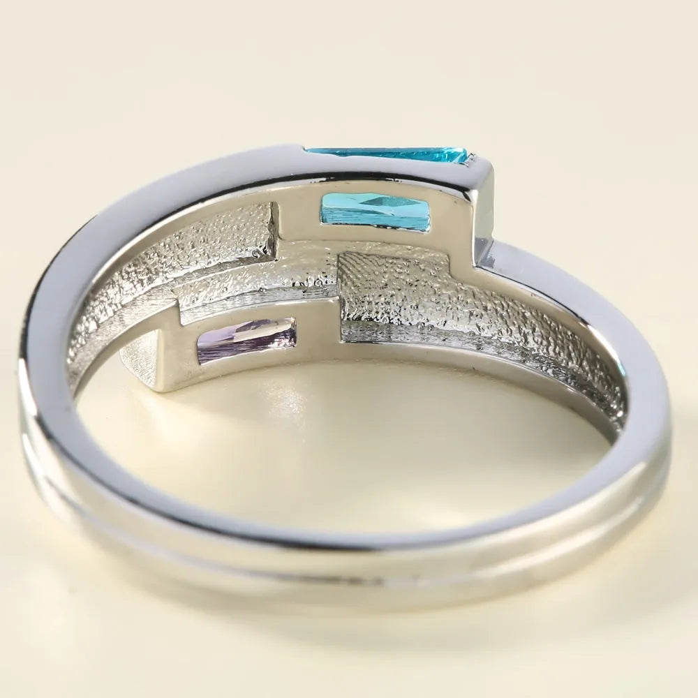 Silver coloured copper electroplated ring with a central zircon stone, shown on a finger.