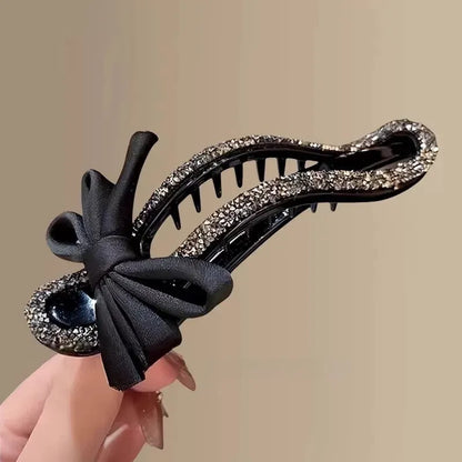 A black crystal bow on a clear 11.5cm long acrylic banana hair clip with bobby pin back.
