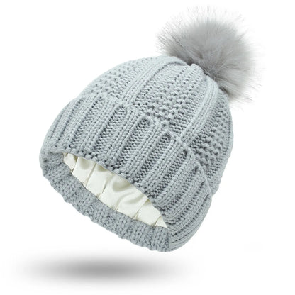 Woman wearing a wine red wool beanie hat with a faux fur pom pom and satin lining.