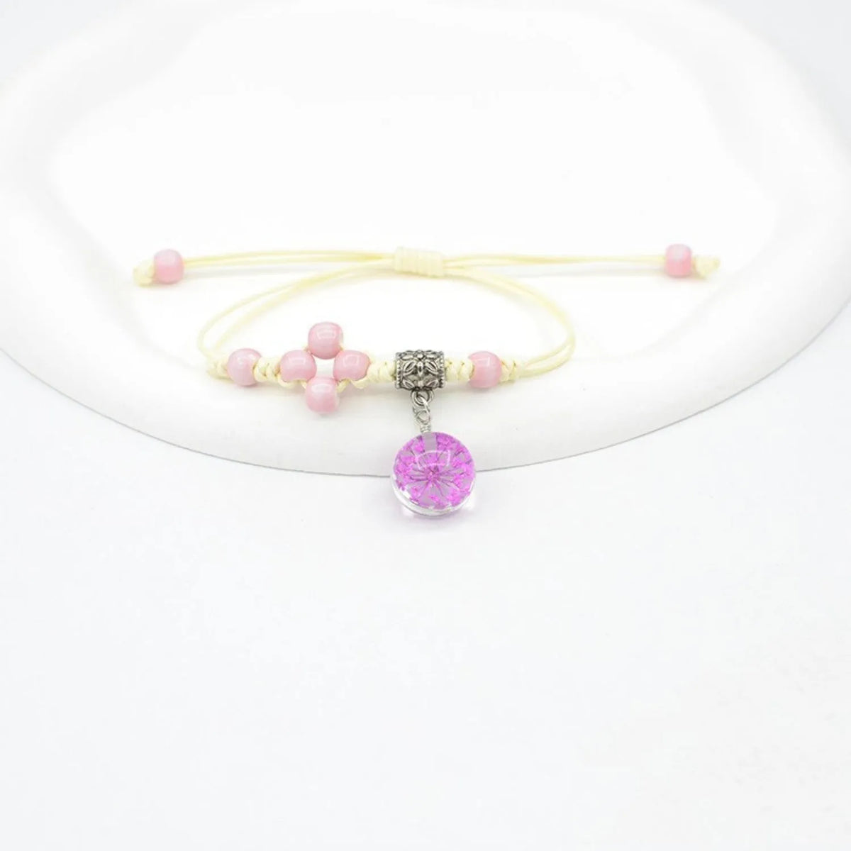 Close-up of a hand-woven bracelet with a large 1.4cm glass bead containing colourful dried flowers.