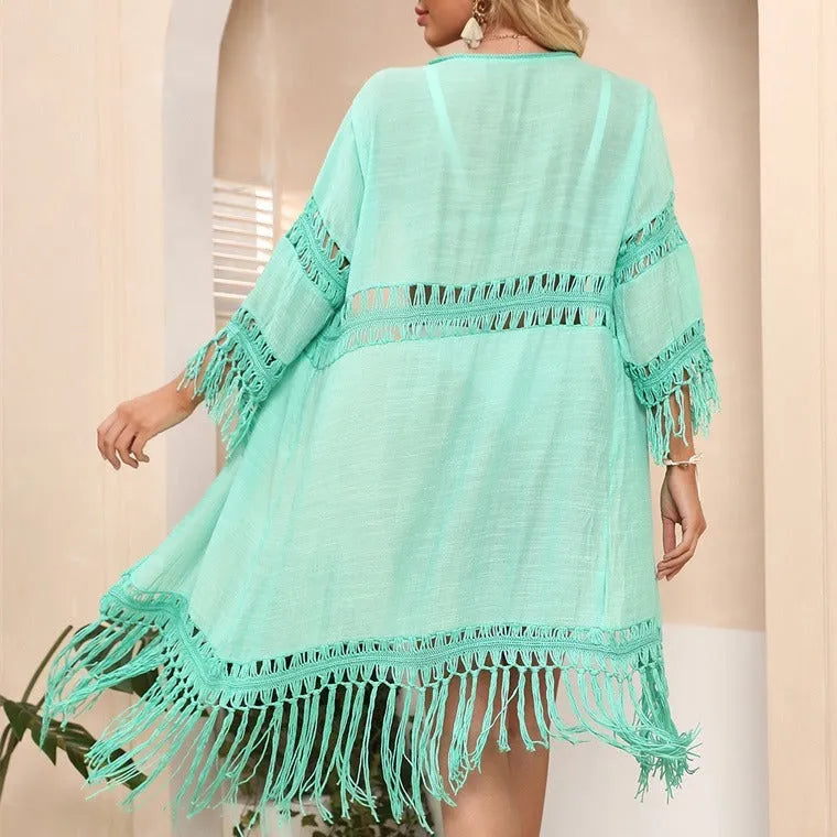 Yellow hand-crocheted acrylic beach cover-up cardigan with tassels, laid flat on a sandy background.