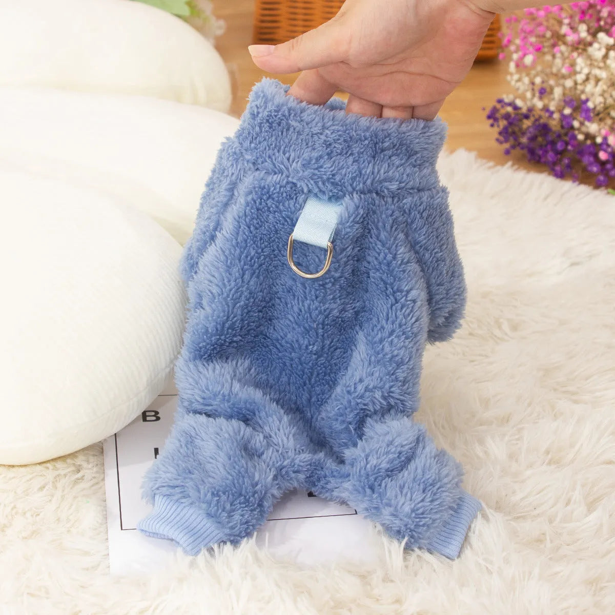 A dog wearing a blue, double-sided plush, four-legged coat with a high collar and a small towing ring visible.