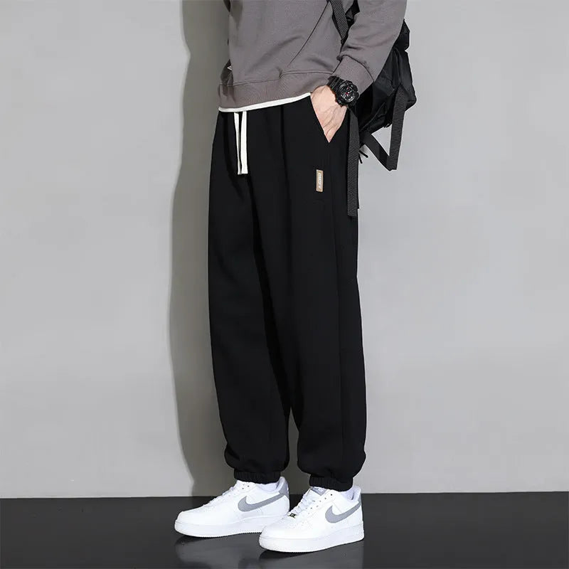 Man wearing loose grey sports trousers with an elasticated drawstring waistband.