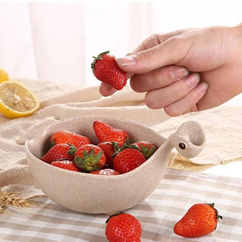 Three colourful dinosaur-shaped bowls made from wheat straw in pink, green, and beige.